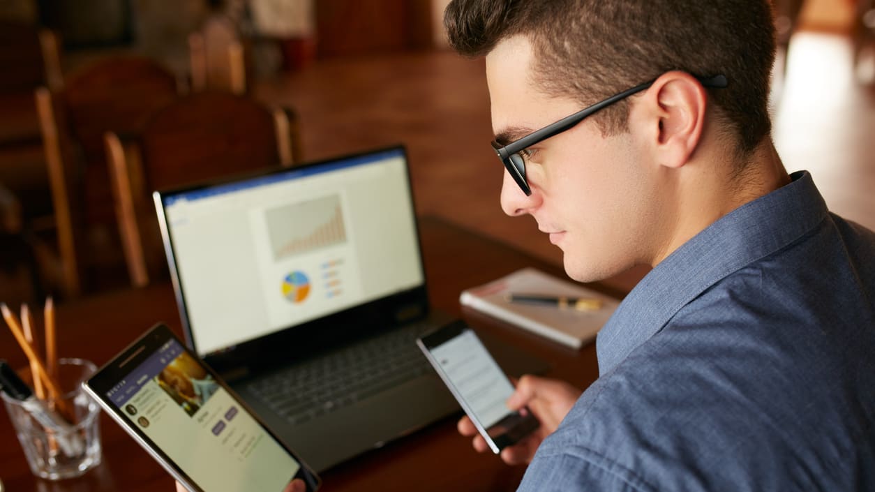 A man sitting at a table with a laptop and cell phone.