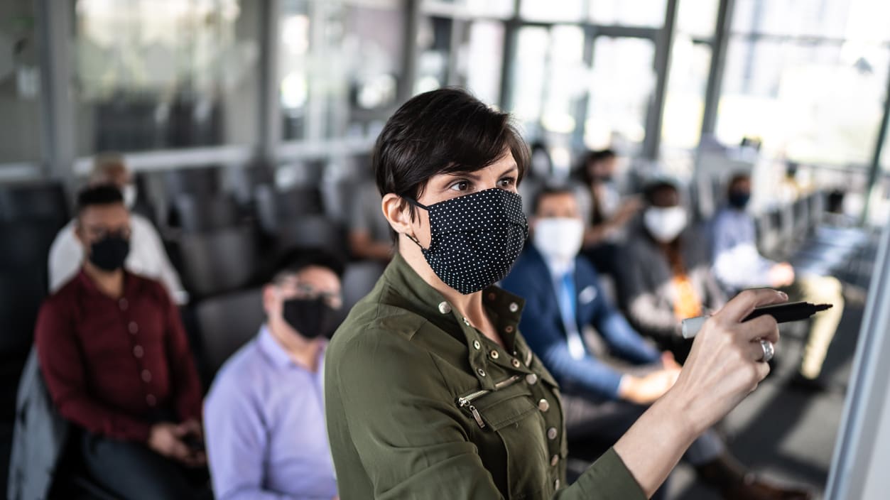 A woman wearing a face mask in front of a group of people.