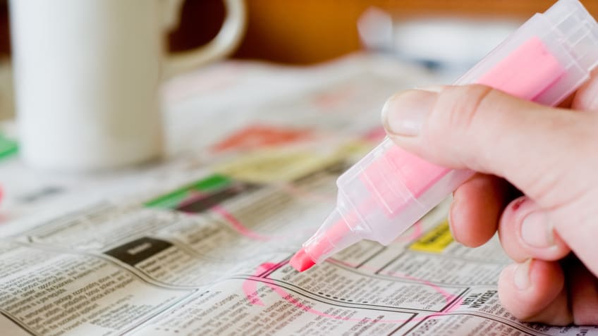A hand holding a pink marker on a newspaper.