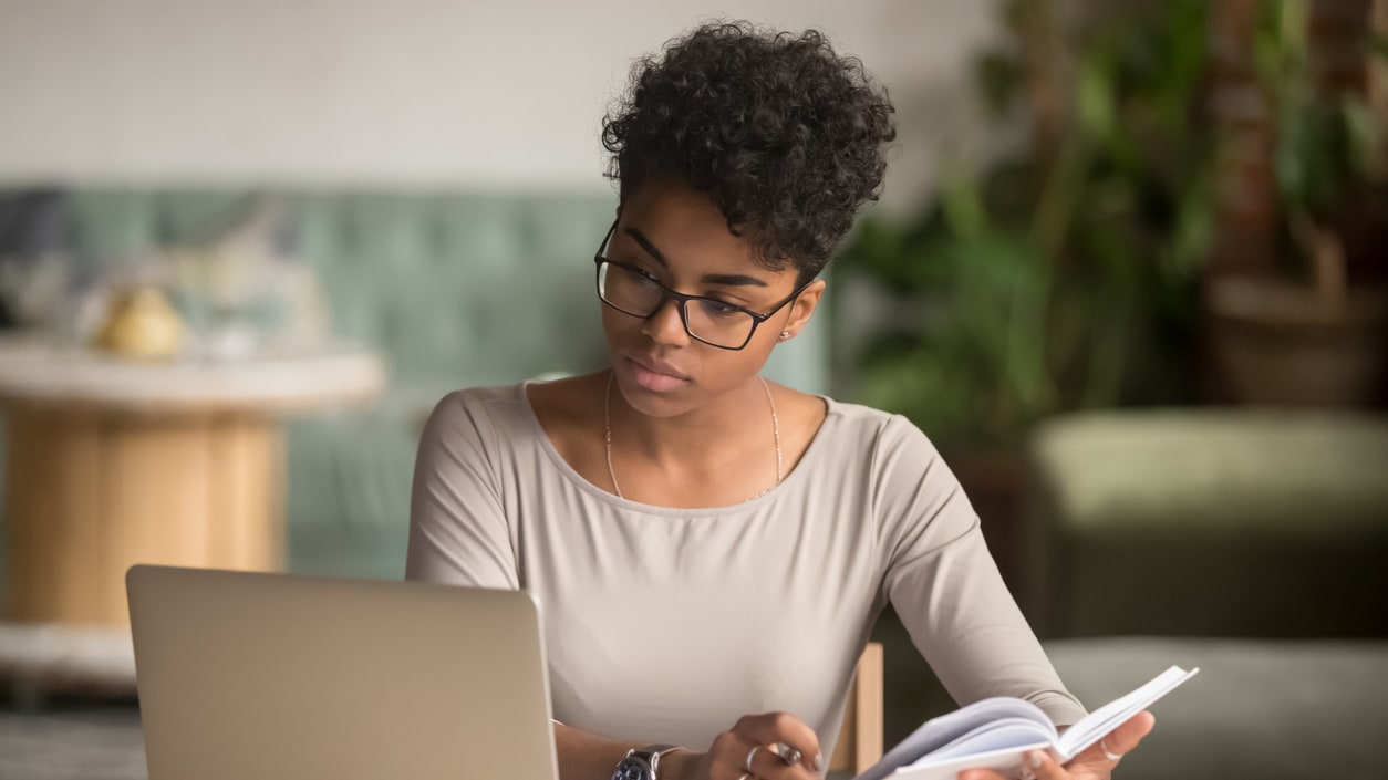 A woman with glasses is working on her laptop at a table.