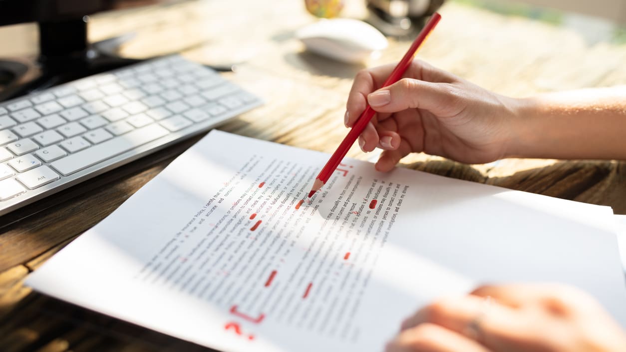 A person writing on a paper with a red pen.