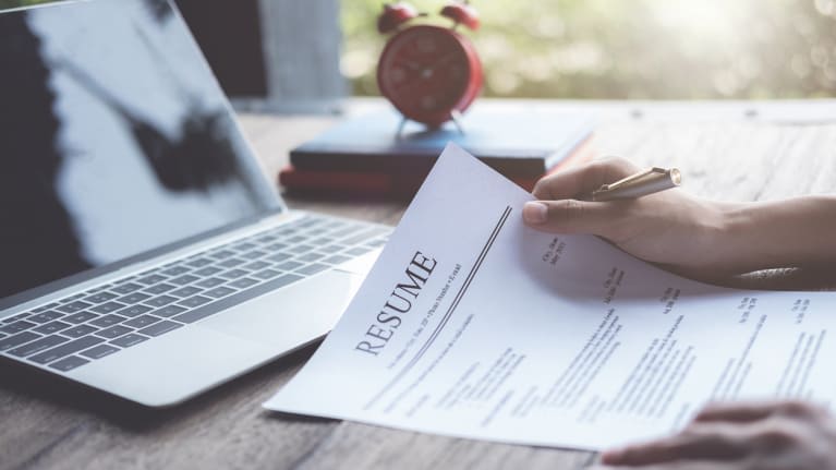 A person writing a resume on top of a laptop.