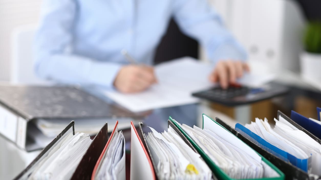 A woman is sitting at a desk with papers and a calculator.