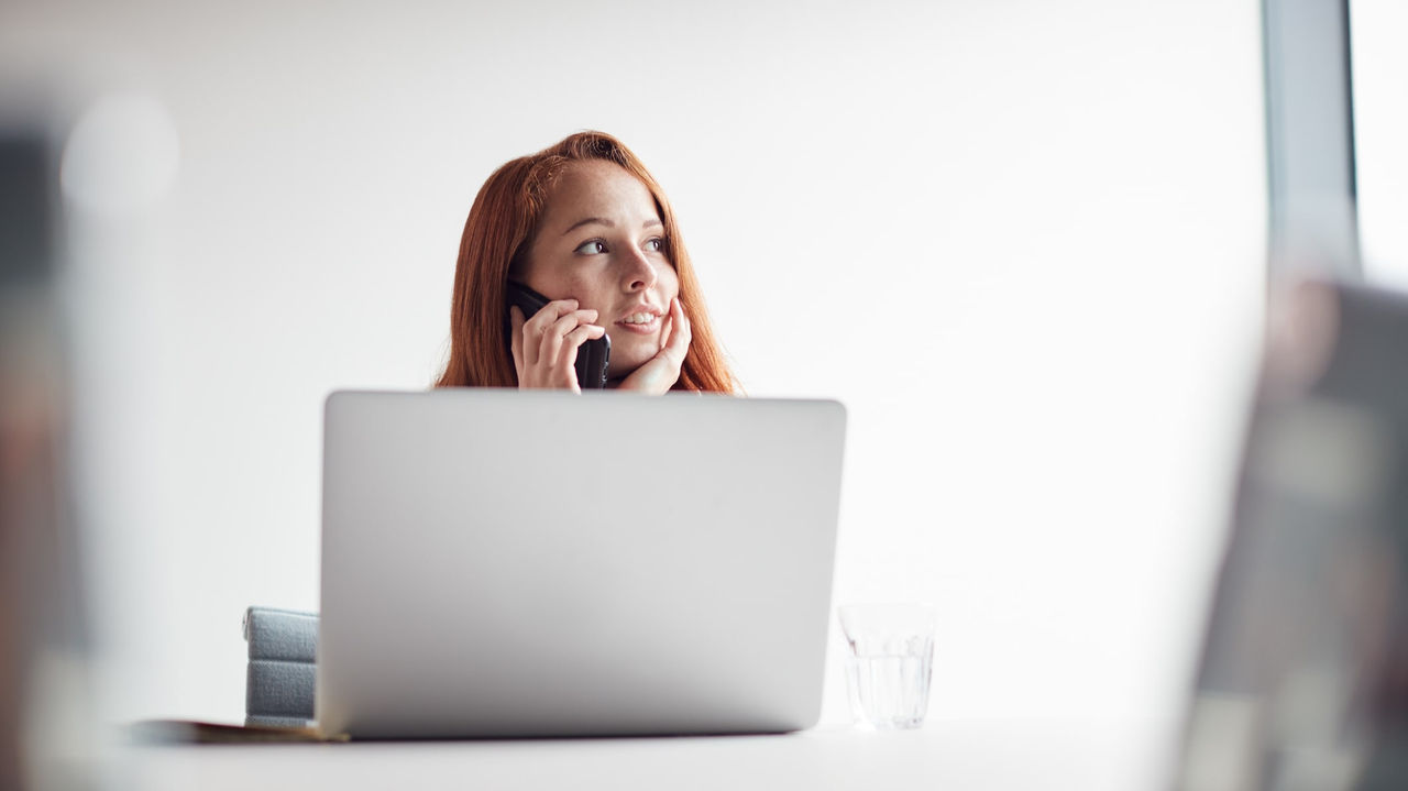 A woman talking on the phone while sitting in front of a laptop.