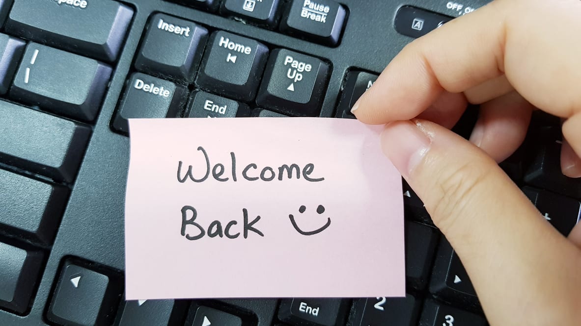 A hand holding a welcome back note on a keyboard.