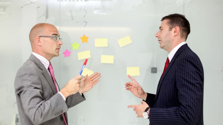 Two businessmen arguing in front of a glass wall.