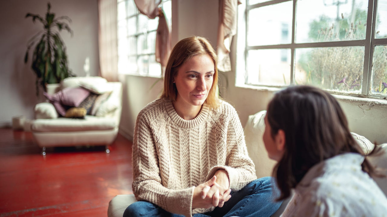 Two women sitting on a couch talking to each other.