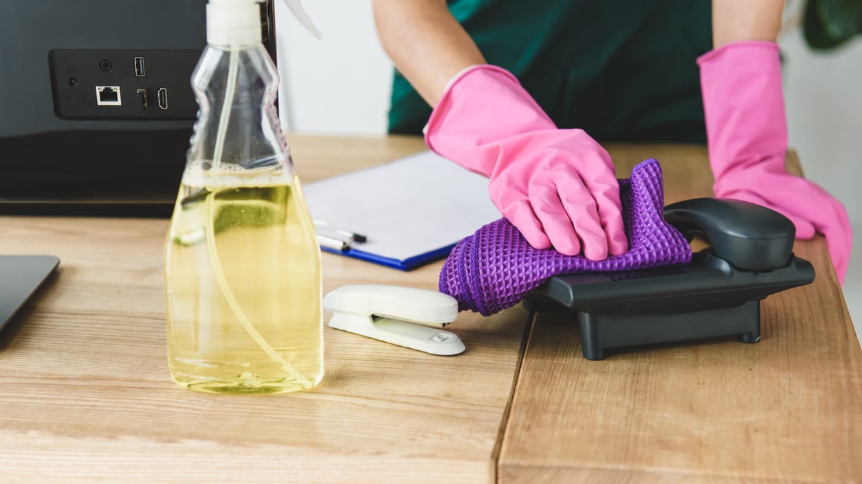 A woman cleaning a desk with a purple cloth.