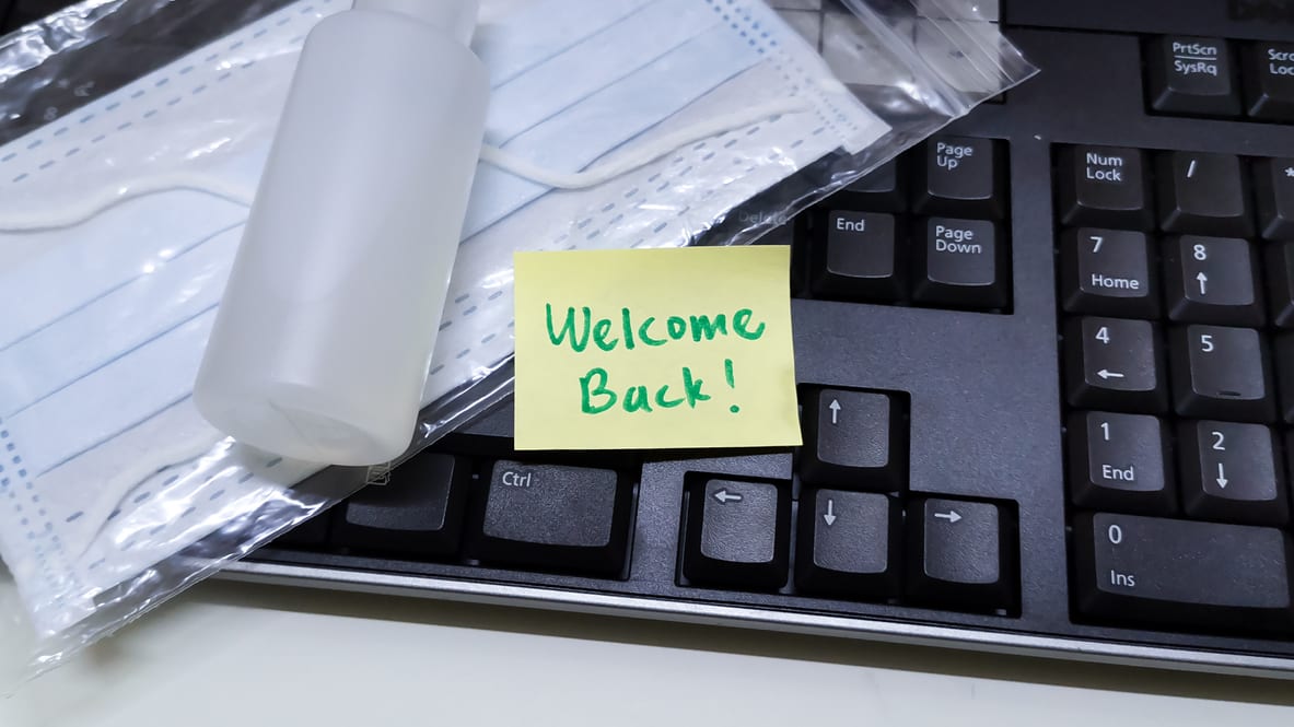 A welcome back note on a keyboard next to a bottle of hand sanitizer.
