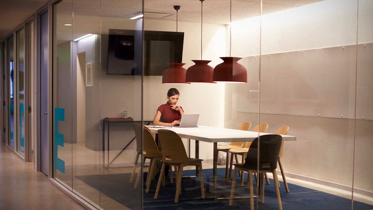 A woman is sitting at a table in a glass office.