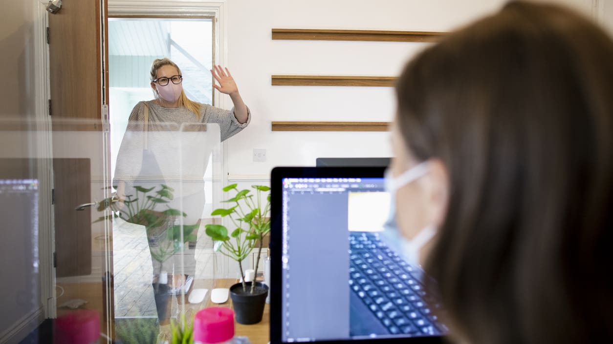 A woman wearing a face mask is standing in front of a computer.