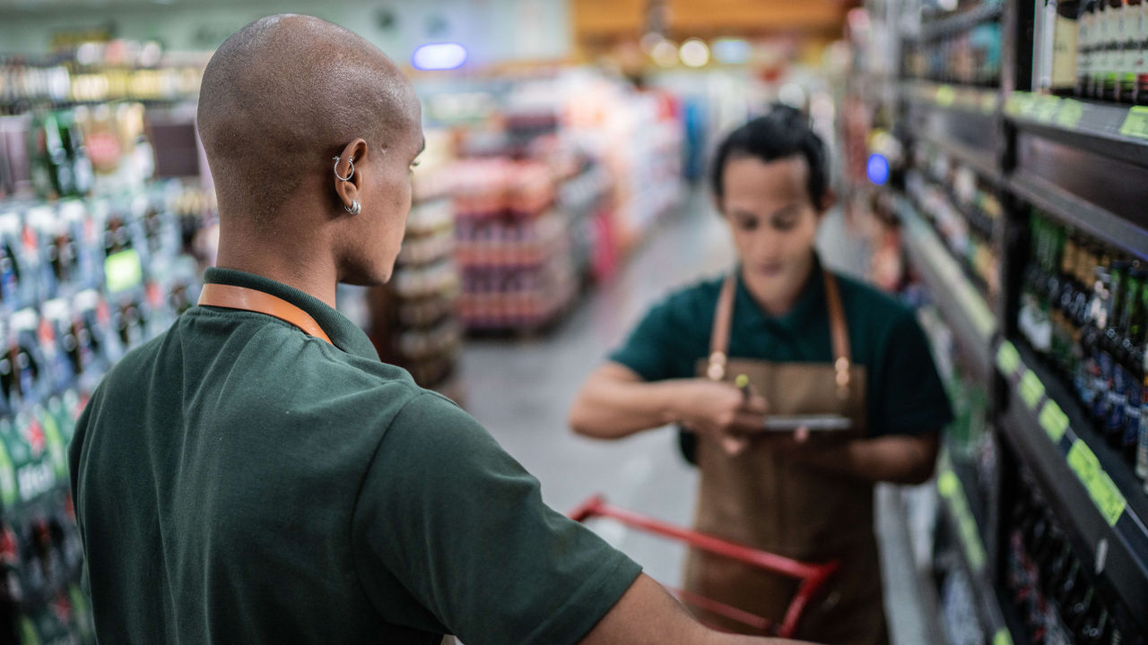 A man in a green apron is standing in a supermarket aisle.