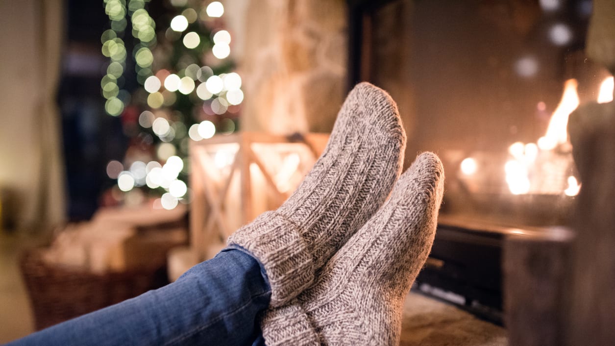 A person's feet in front of a fireplace with a christmas tree in the background.