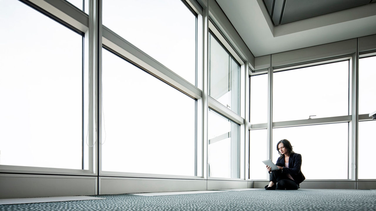 A business woman sitting on the floor in front of a large window.