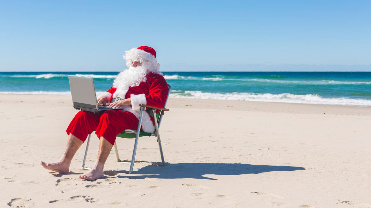 A santa claus sitting on the beach with a laptop.