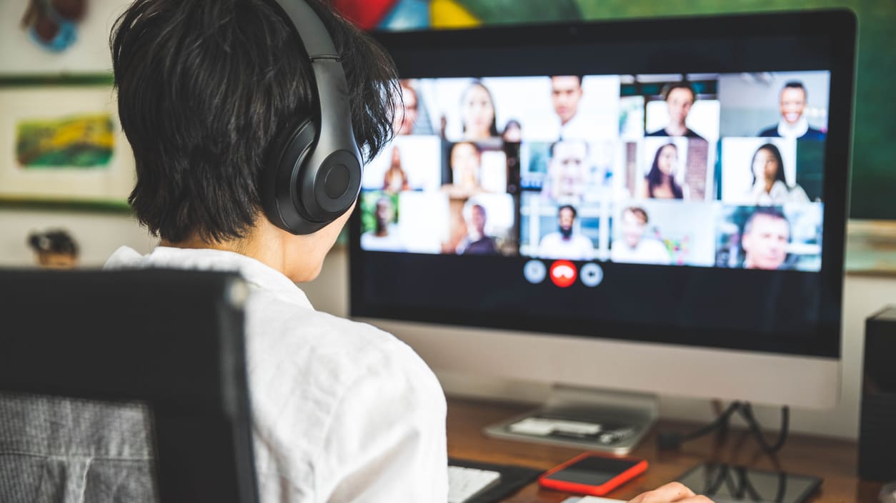 A person wearing headphones is watching a video conference on a computer.