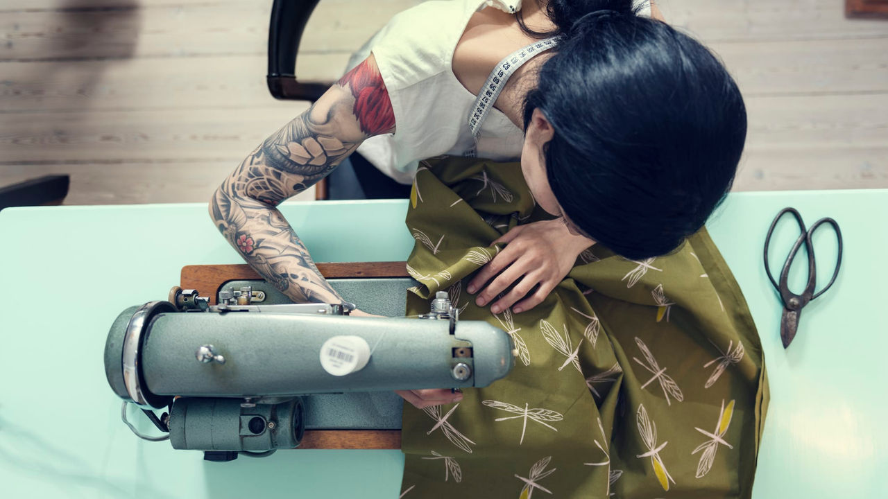 A woman with tattoos working on a sewing machine.