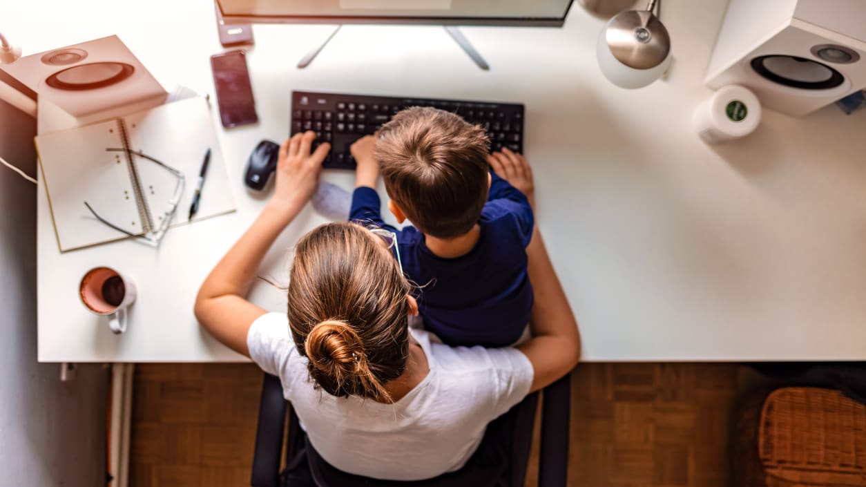 A woman and a child sitting at a desk using a computer.