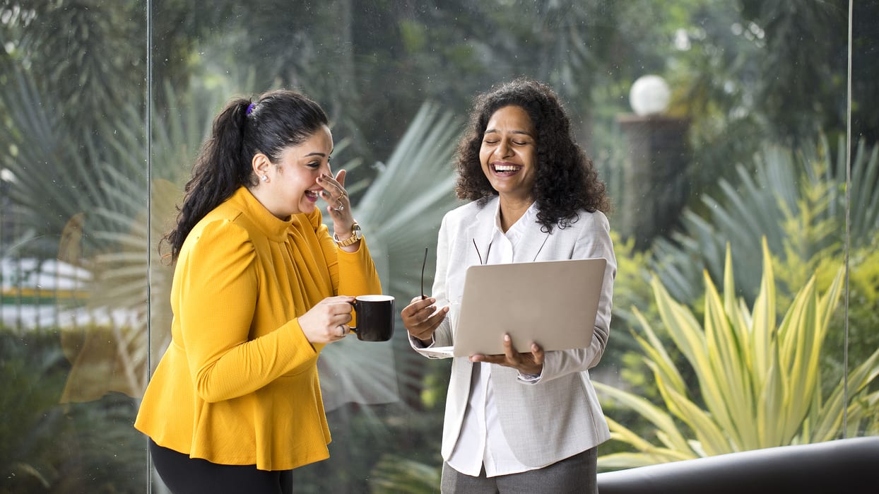 Two business women talking while holding laptops in an office.