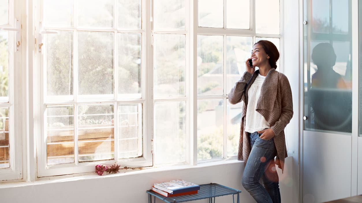 A woman standing in front of a window talking on her cell phone.