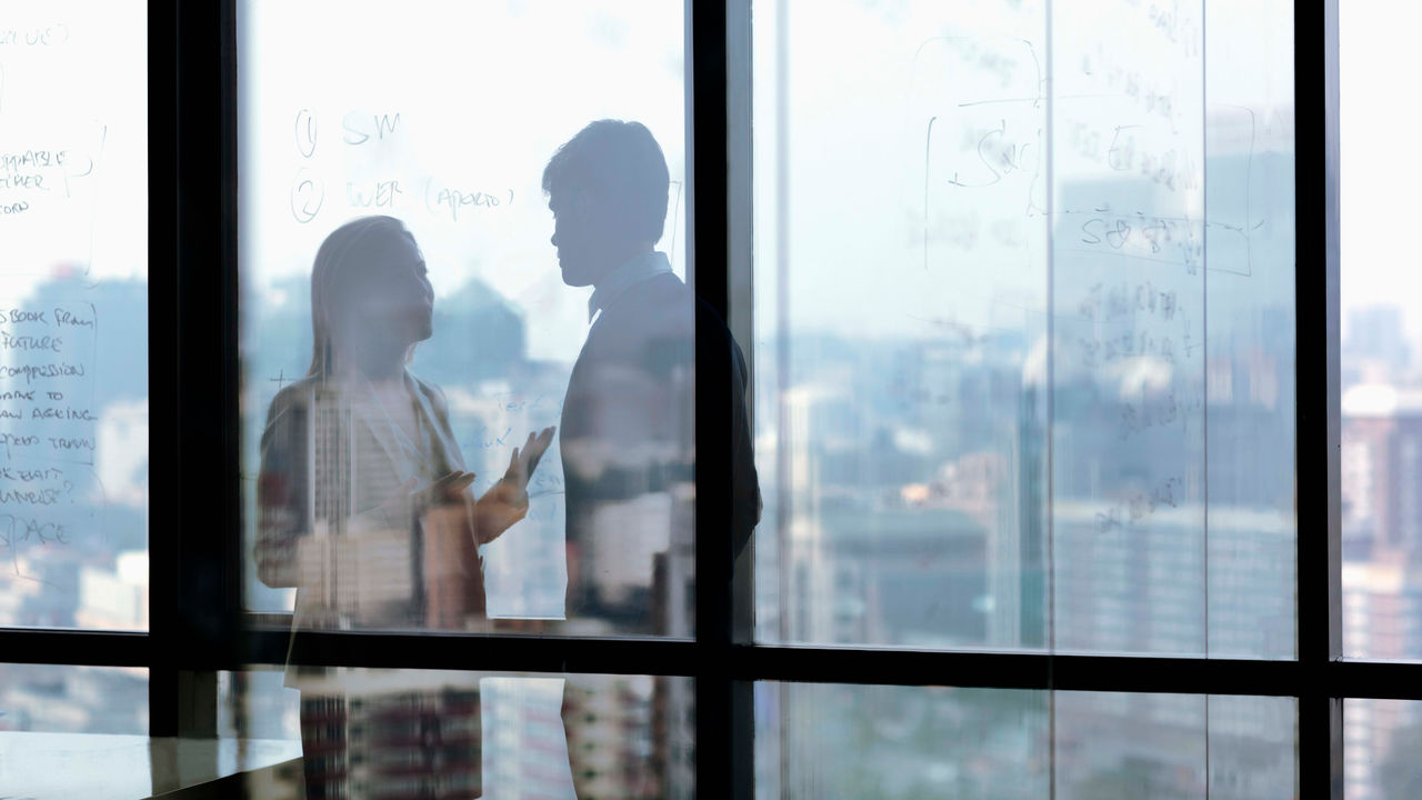 Two people standing in front of a window with writing on it.