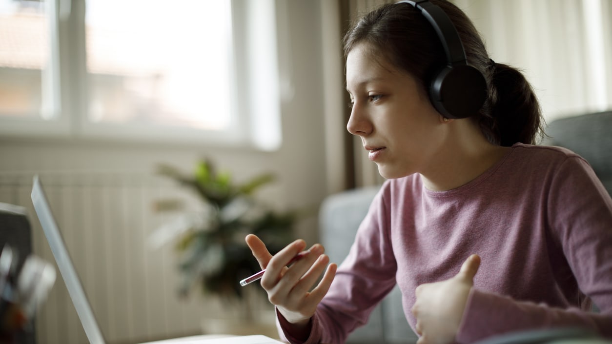 A young woman is using a laptop while wearing headphones.