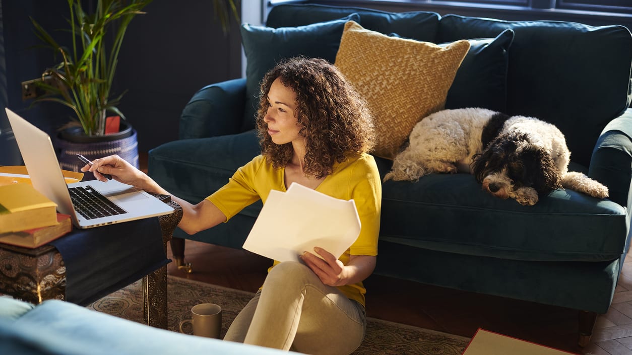 A woman sitting on a couch with a laptop and a dog.