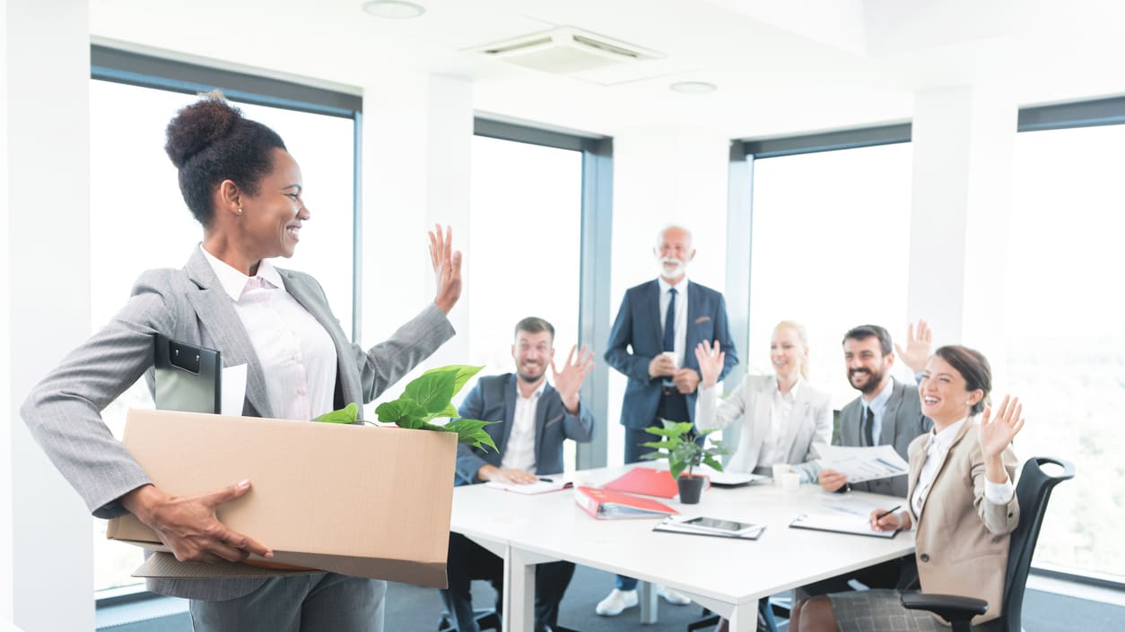 A woman in a business suit holding a box in front of a group of people.