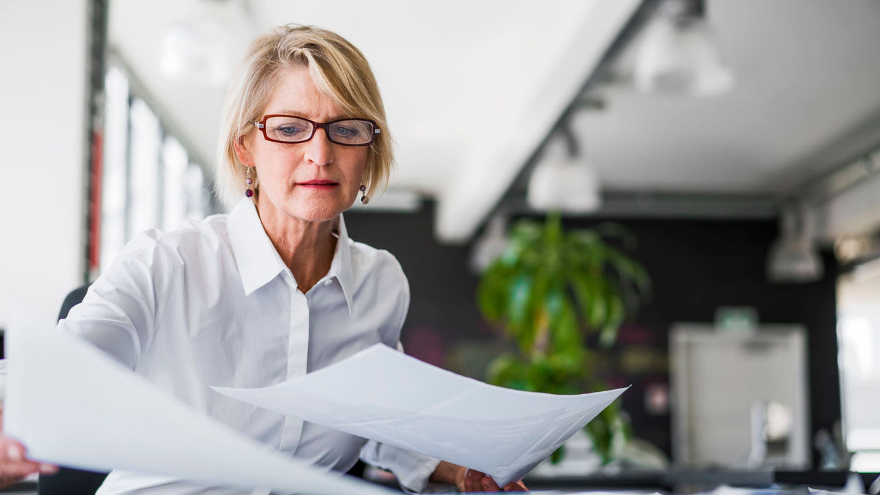 A woman in glasses is looking at a piece of paper.