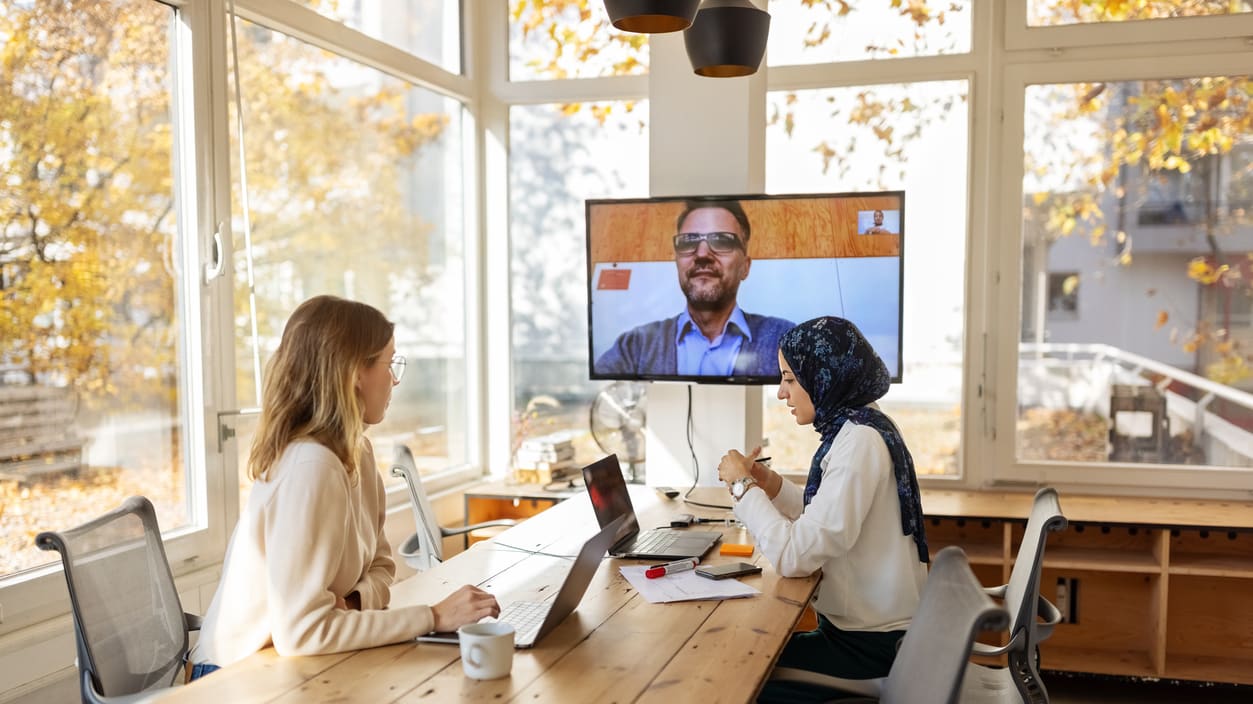 A group of people sitting at a table and watching a video on a tv.