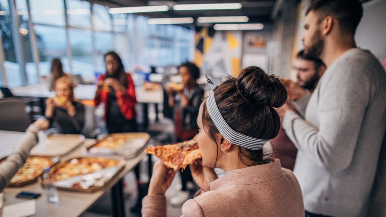 A group of people eating pizza in an office.