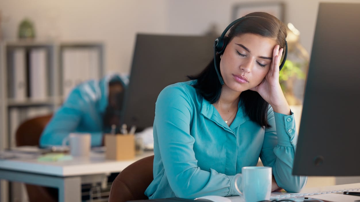 A woman in a blue shirt is sitting at a desk with her head resting on her head.