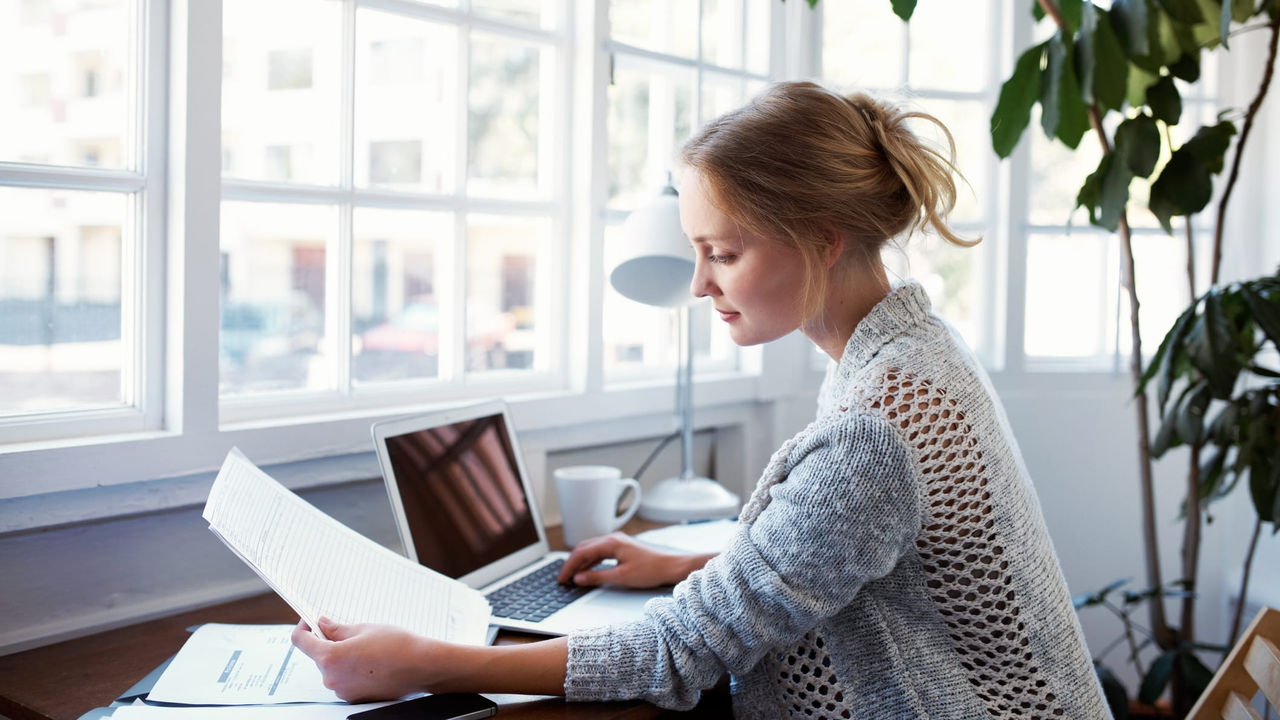 A woman sitting at a desk with a laptop in front of a window.