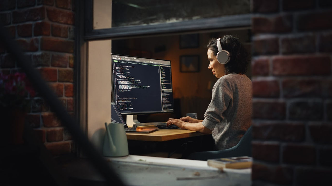 A woman is working on a computer in front of a brick wall.