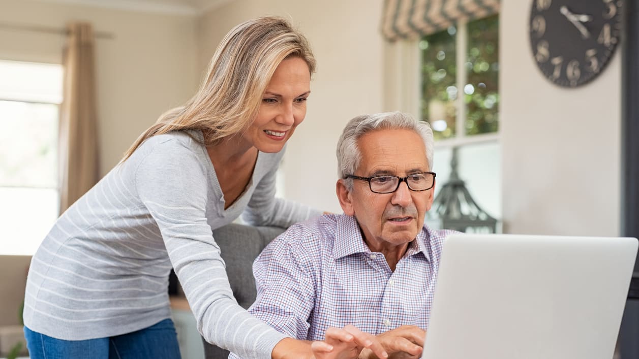 A woman is helping an older man on a laptop.