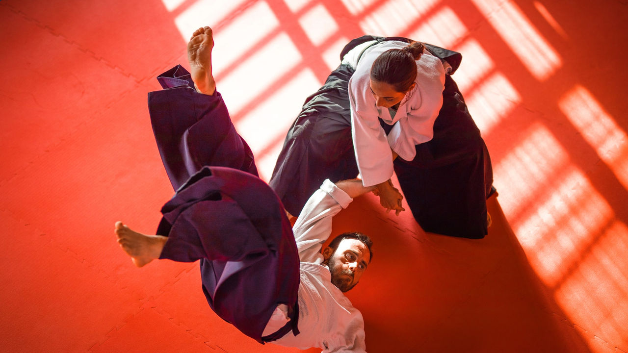 Two men practicing karate on a red floor.