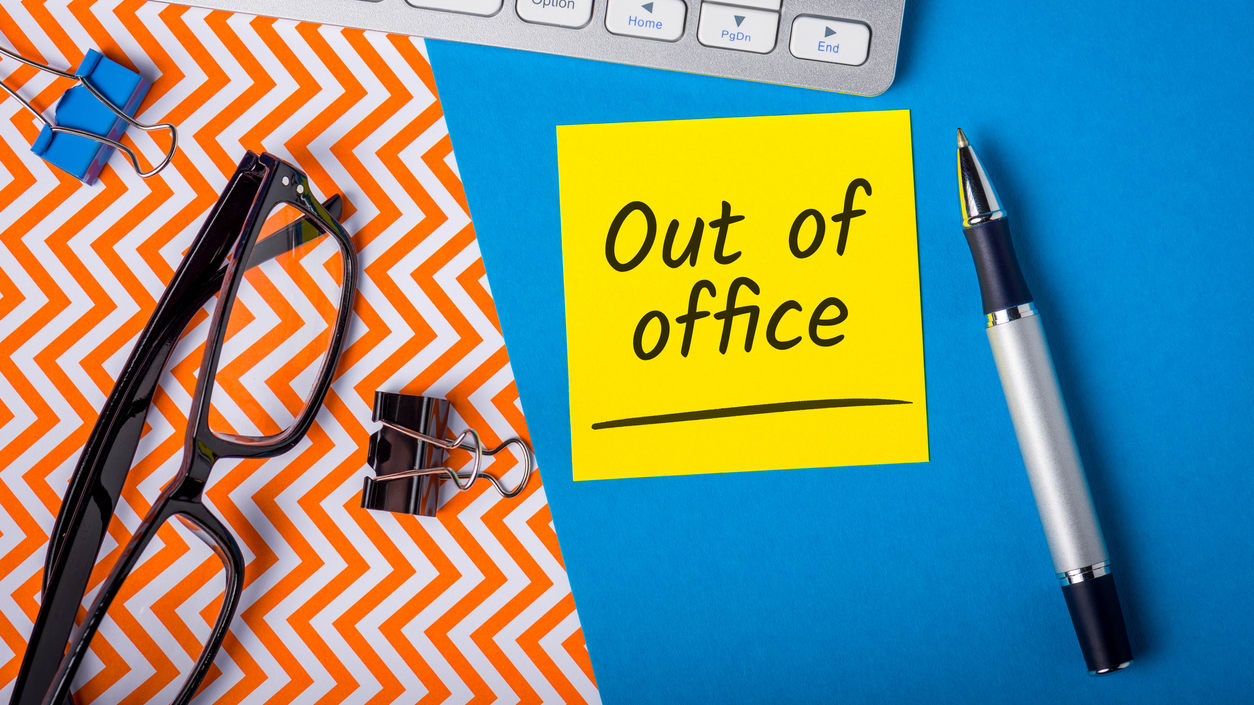 Out of office note on a desk with a keyboard and glasses.
