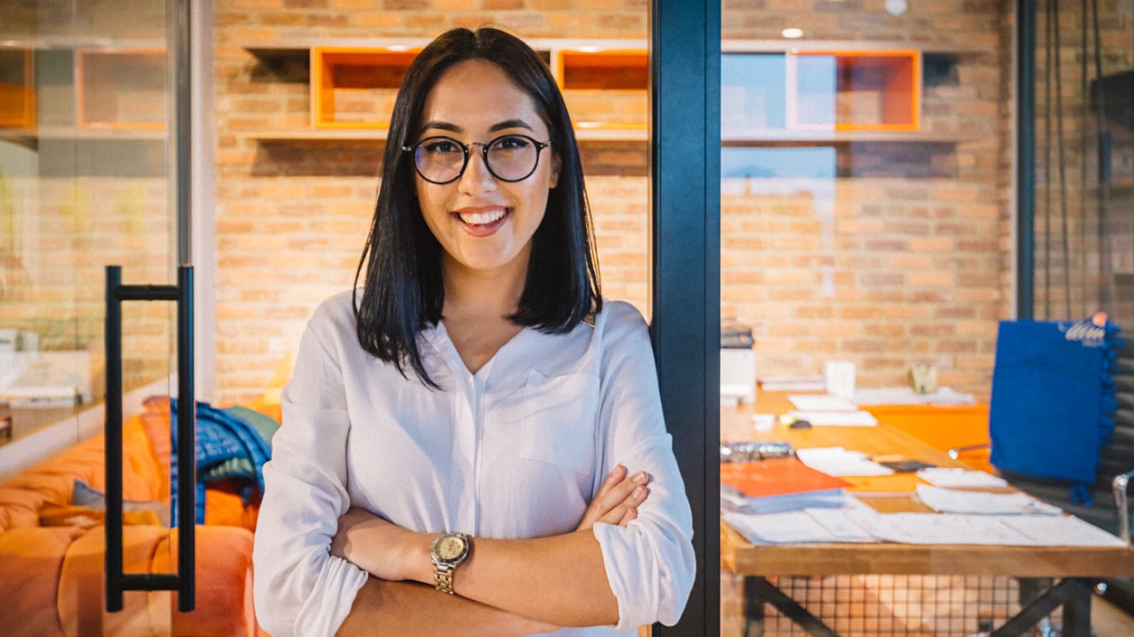 A smiling woman standing in an office with her arms crossed.