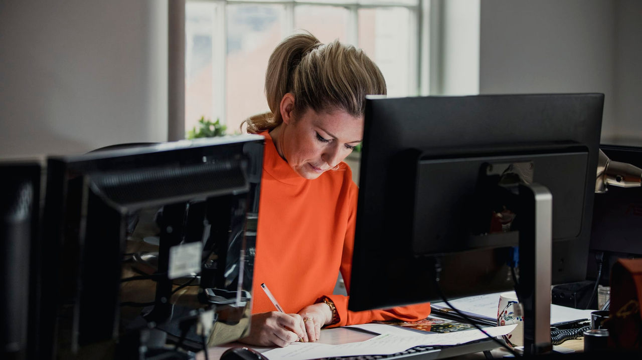 A woman working at a desk in front of two monitors.