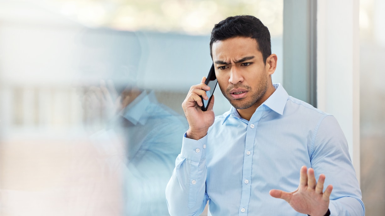 A man talking on the phone while standing in front of a window.