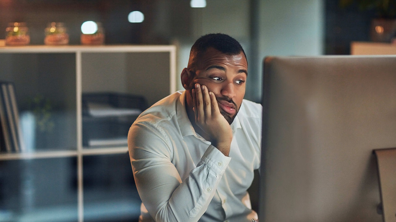 A man sitting in front of a computer with his hand on his face.