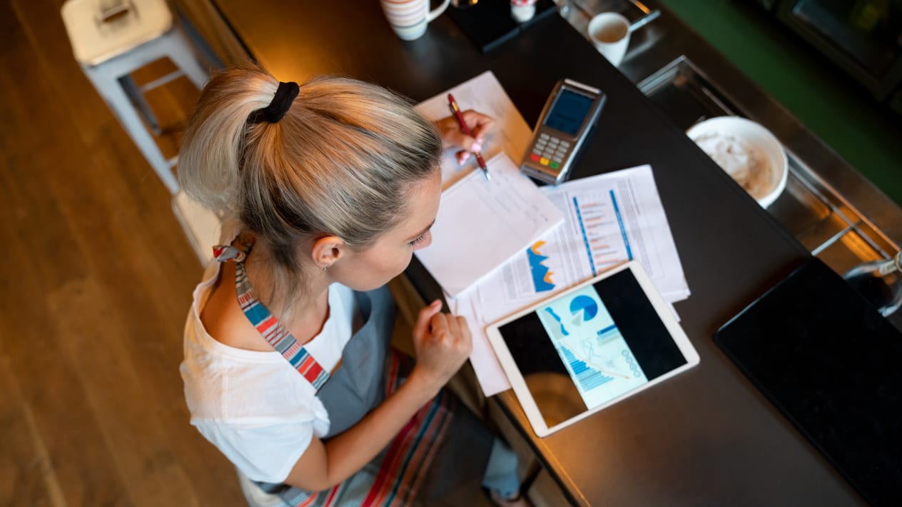 A woman sitting at a table with a tablet and papers.