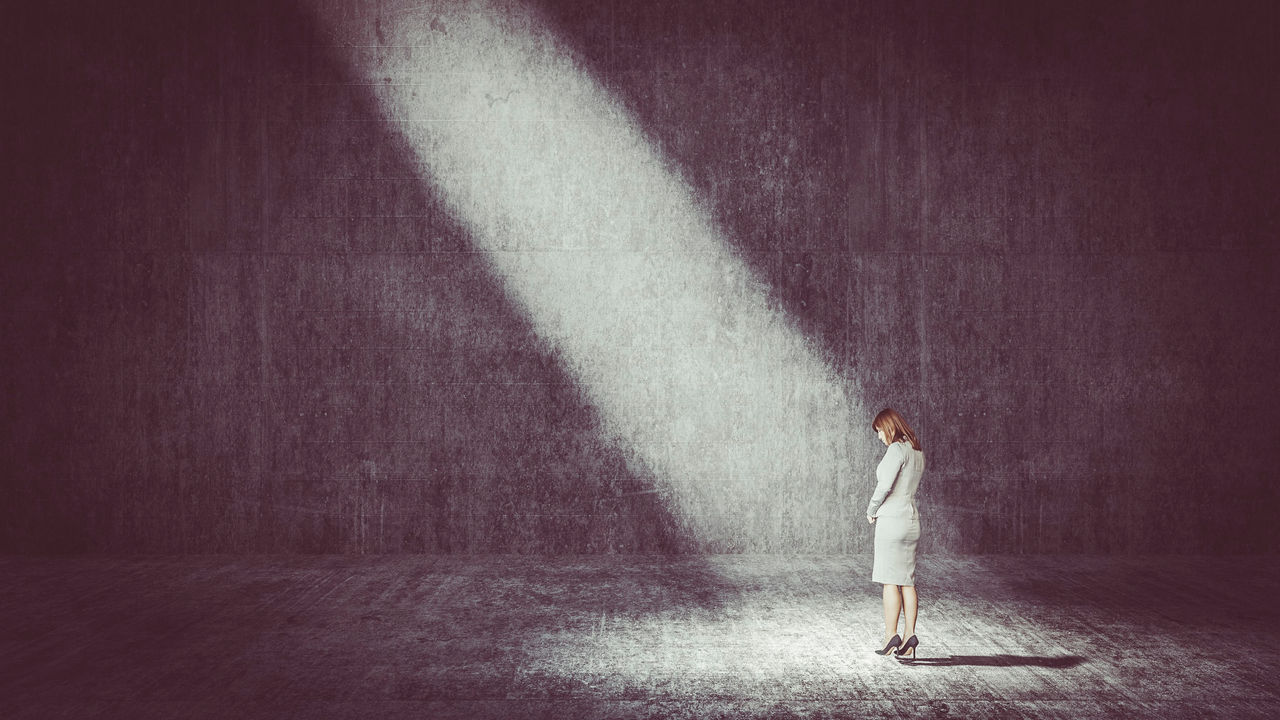 A business woman standing in front of a light beam in a dark room.