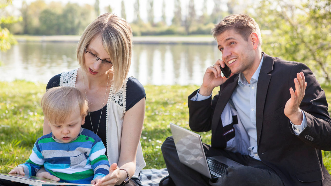 A family with a baby sitting on a blanket in a park.