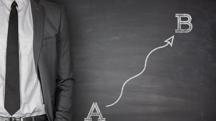 Businessman standing in front of a chalkboard with an arrow pointing up.