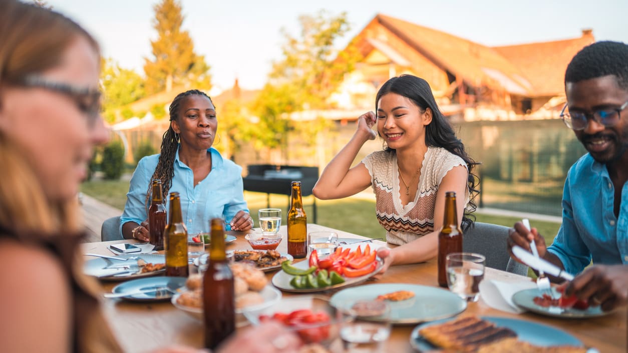 A group of people sitting around a table at a backyard barbecue.