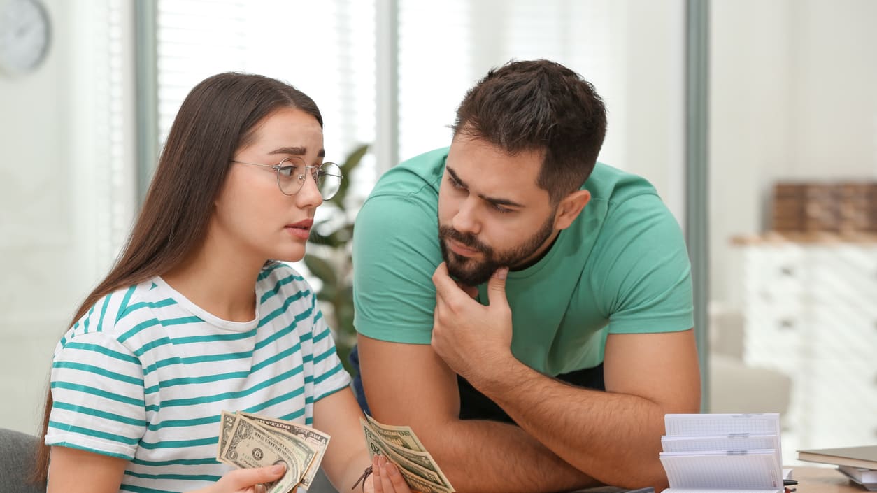 A man and woman sitting at a desk and looking at money.