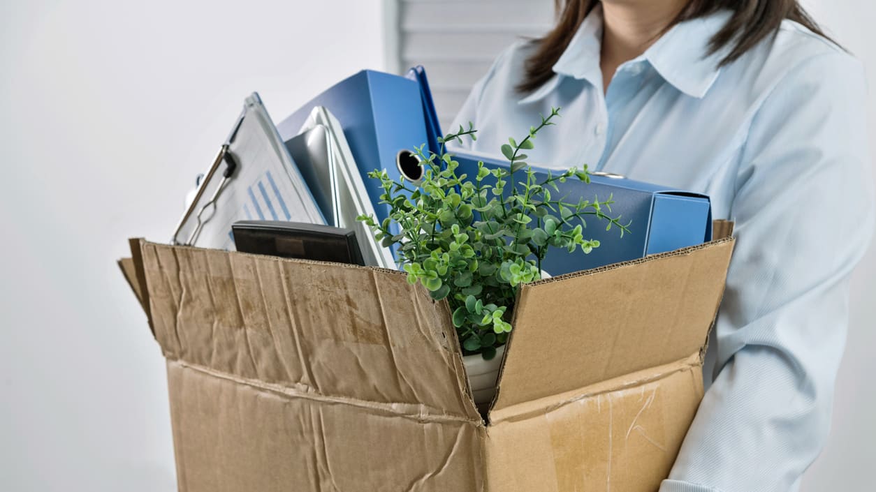 A woman carrying a cardboard box full of office supplies.