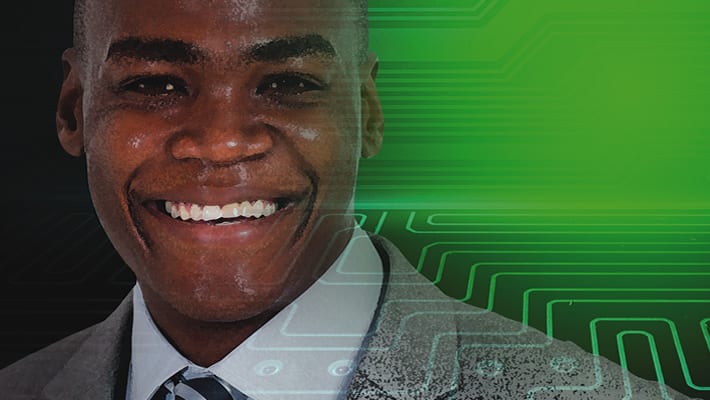 A man smiling in front of a green circuit board.