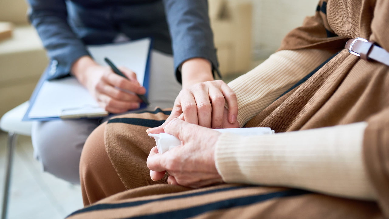 A woman is holding an elderly woman's hand in a doctor's office.